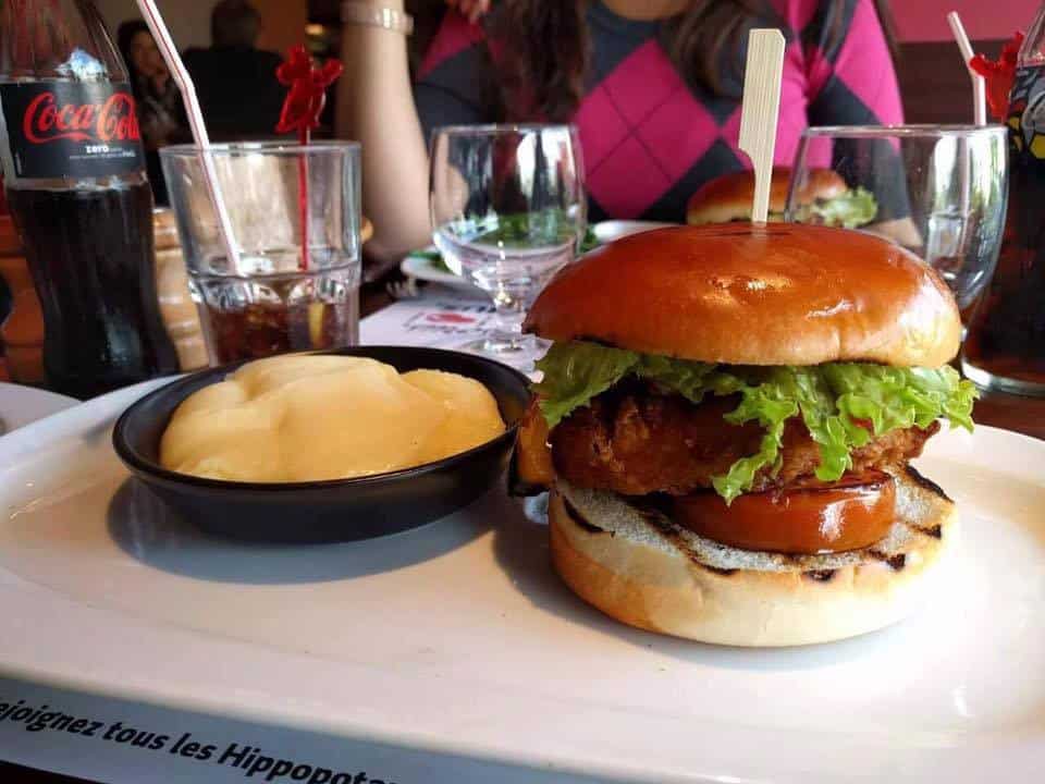 Hippopotamus - Un burger poulet mariné croustillant ,légumes marinés , tomate fraîche, sauce pesto, rondelles d’oignon rouge et salade mélangée