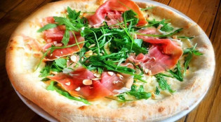 AntePrima - La pizza base de crème, composée d'un succulent mélange de fromages de mozza fior di latte et de fromage de chèvre, accompagnée de jambon de Parme de 18 mois d'affinage, d'amandes torréfiées, de miel et recouverte de roquette